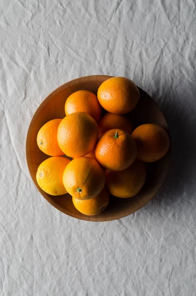 Portakal beyaz keten masa örtüsü üzerinde ahşap bir kasede.