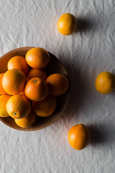 Portakal beyaz keten masa örtüsü üzerinde ahşap bir kasede.