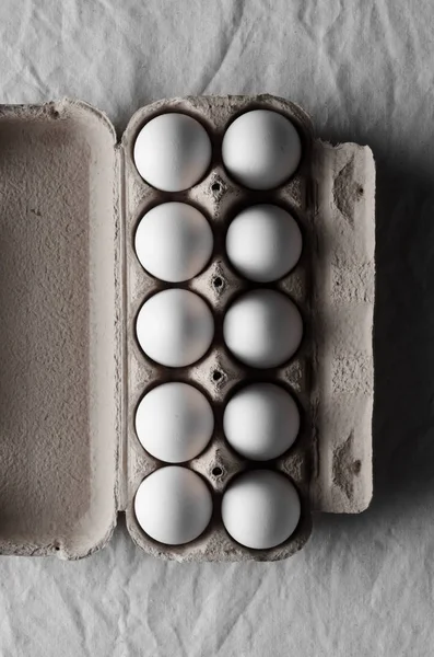 White eggs in an egg carton. White linen tablecloth background.