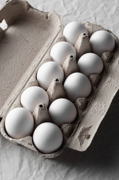 Bir yumurta kartonu beyaz yumurtalar. Beyaz keten masa örtüsü arka plan.