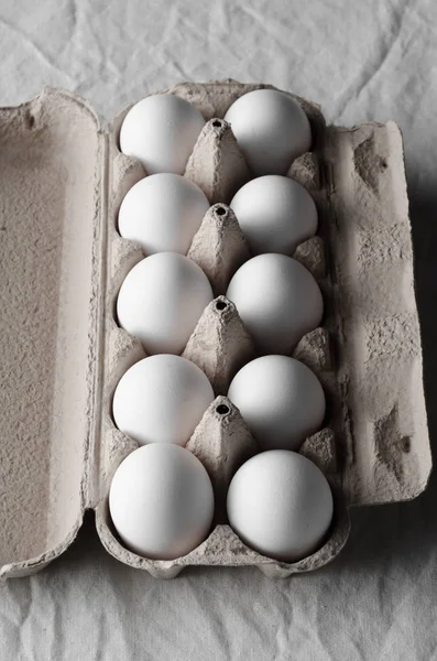 White eggs in an egg carton. White linen tablecloth background.