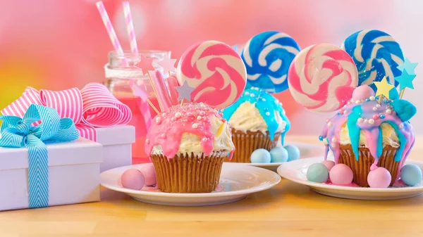 Three pink and blue novelty cupcakes decorated with candy and large lollipops. — Stock Photo, Image