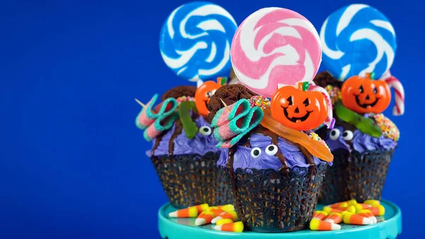 Halloween candyland drip cake style cupcakes with candy on blue background. — Stock Photo, Image