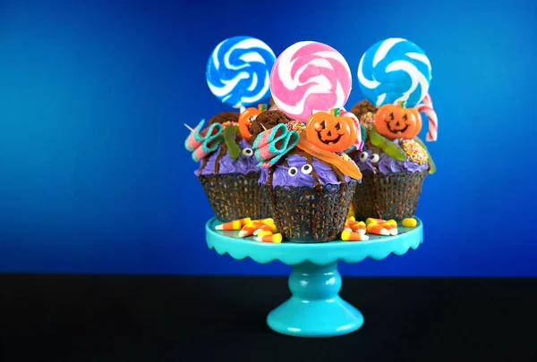 Halloween candyland drip cake style cupcakes with candy on blue background.