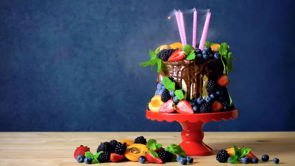 Chocolate drip cake decorated with fresh berries and candles blown out.