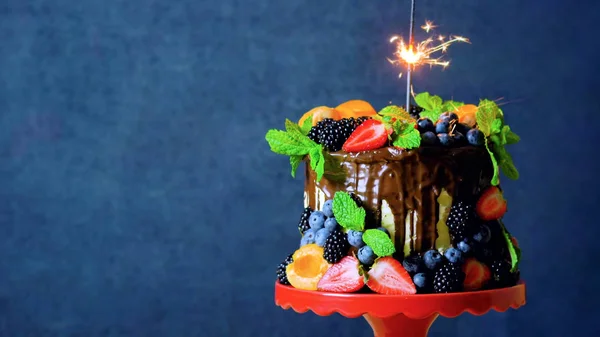 Chocolate drip cake decorated with fresh fruit and berries with copy space.