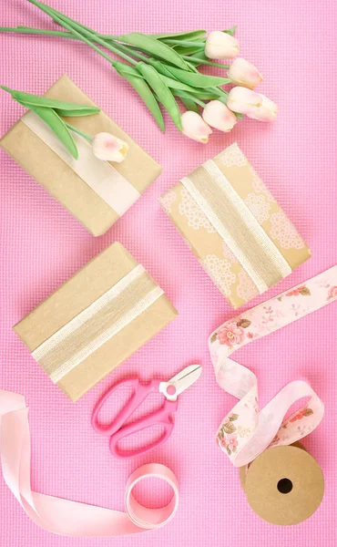 Gifts wrapped in kraft paper and pink ribbons overhead flatlay. — Stock Photo, Image