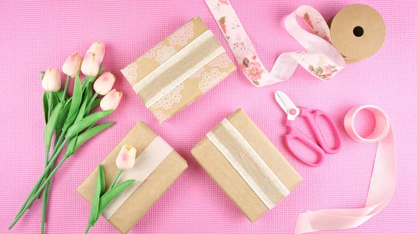 Gifts wrapped in kraft paper and pink ribbons overhead flatlay. — Stock Photo, Image