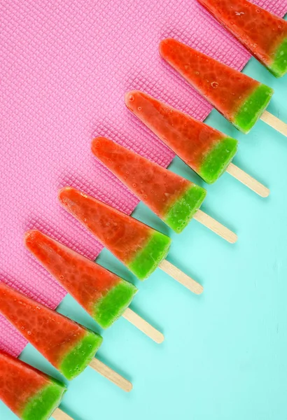 Watermelon flavored summer ice cream popsicles on pink and blue background.