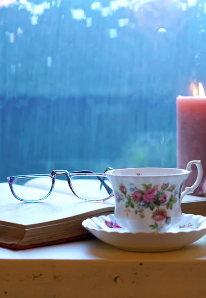 在寒冷的雨天, 带着书和一杯茶在窗边放松身心. — 图库照片