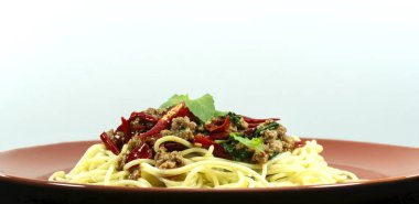 Spagetti Fried Basil ile karıştırın domuz beyaz arka plan üzerinde bir çanak kahverengi sahne dekorasyon kırmızı biber kıyılmış, kopya alanı, yakın.