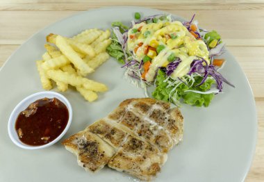 Biftek bir ahşap arka plan dekorasyon kızarmış patates, yeşil salata, mor karnabahar, üstten görünüm üzerinde beyaz bir tabak içinde baharatlı soslu tavuk.