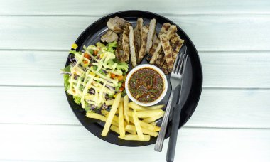 Beyaz ahşap zemin arka plan sahne dekorasyonu ile yeşil salata, mor karnabahar, üstten görünüm, kopya alanı üzerinde siyah bir tabak içinde domuz eti biftek ve Patates kızartmak.