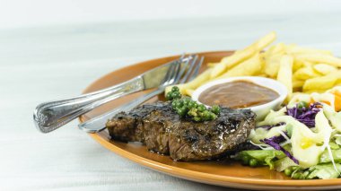 Sığır eti biftek ve Patates kızartma bir kahverengi beyaz arka plan sahne dekorasyon yeşil salata, mor karnabahar, açık görüş, kopya alanı ile çanak