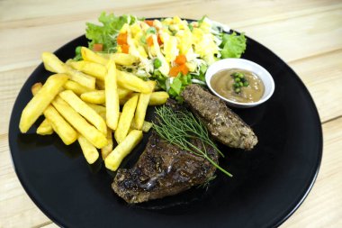 Ahşap zemin arka plan sahne dekorasyonu, kızarmış patates ve et suyu sosu ile yeşil salata, mor karnabahar, kopya alanı üzerinde siyah yemek sığır eti biftek.