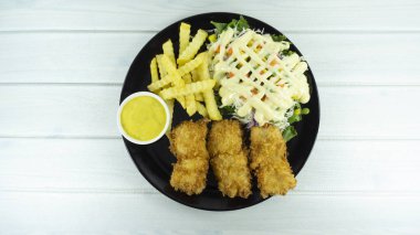 Siyah bir tabak kızarmış balık biftek bir beyaz ahşap zemin tablo baharatlı sos ve patates kızartması, yeşil salata, mor karnabahar, metniniz için kopya alanı görünümüyle Top.