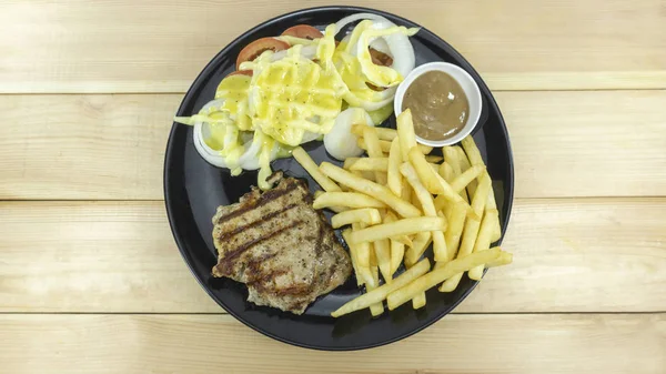 Beef steak in black dish and French Fries on wood table props decoration Gravy Sauce with Onion,tomato,top view Copy Space.