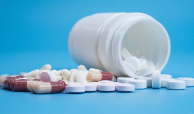 Birçok Toplu beyaz haplar Anti-virüs COVID-19 mavi arka plandaki ilaç şişesinden, Cephe Görünümü Boşluğu tasarım alanı için.