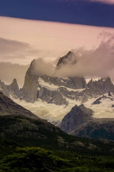 Rocky snowy mountain peaks with the sun rising behind and red clouds. Fitz Roy in Argentina