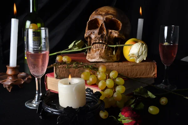 Naturaleza muerta con una calavera con rosas, libros, frutas, vino y velas sobre un fondo oscuro