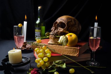 Naturaleza muerta con una calavera con rosas, libros, frutas, vino y velas sobre un fondo oscuro