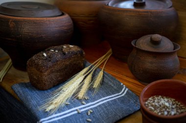 Çavdar ekmeği, seramik kapların arka planına serpiştirilmiş gri bir peçeteye serpiştirilmiş tohumlar serpiştirilmiş.