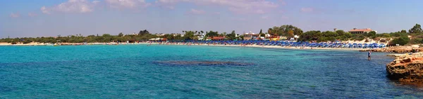 Ayia Napa Kıbrıs Adası plaj geniş panoraması: açık deniz, volkanik sahil, beyaz kum plaj, şezlong ve banyo insanlar, tekneler - panoramik tatilcilerin güneşlenmek