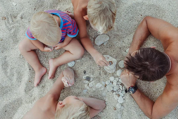 Family are building a pyramid of stones on the beach in the sunset light of the