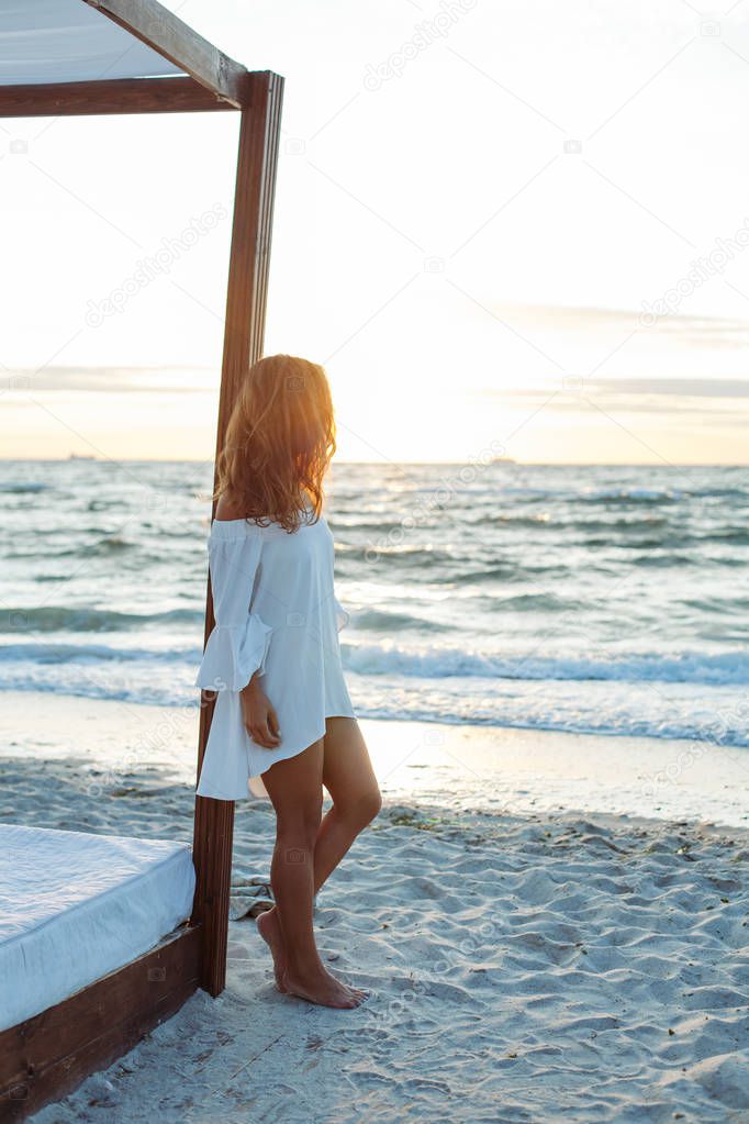 Pretty young sexy woman walking and posing near the ocean at sunrise