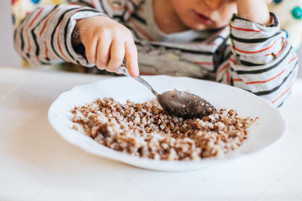 Little boy eats buckwheat porridge himself