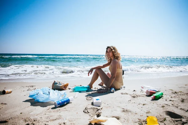 Sahilde farklı plastik çöp Ile kıyı kirliliği. Çöp arasında oturan kadın