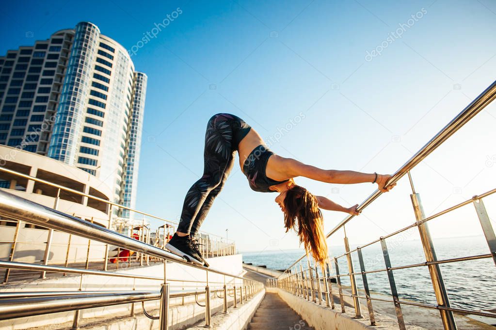Side view of sportswoman performing yogic pose balancing on bridge railings.