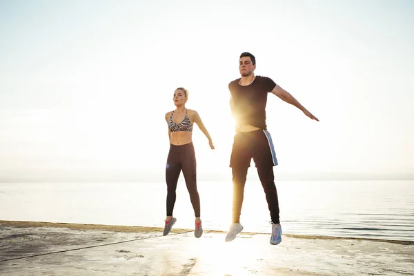 Fitness, sport, friendship and lifestyle concept - couple exercising at the beach