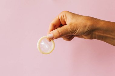 pembe arka plan üzerinde prezervatif tutan kadın el 