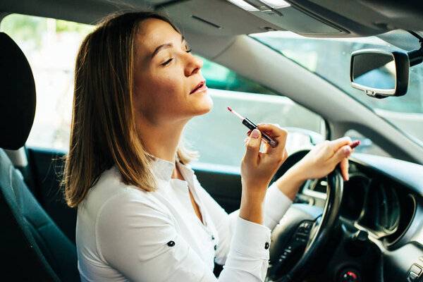 Деловая женщина красит губы в машине
