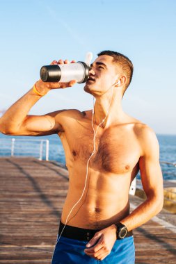 Formda bir adam çok çalıştıktan sonra su içerken telefonunu kullanıyor..