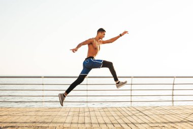 Sportif adam denizin arka planına karşı havada sıçrıyor.