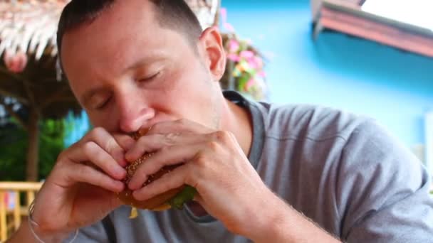 En man biter av en stor hamburgare med nötkött — Stockvideo