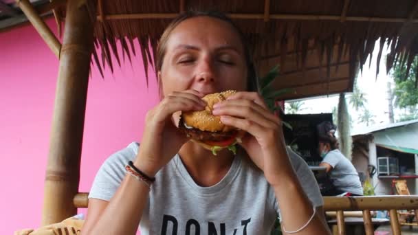 Jong meisje eten veggie hamburger in café in Azië — Stockvideo