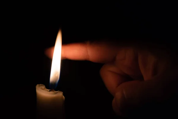 A person takes his finger very close to candle flame behind the flame