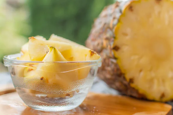 Pineapple pieces and slices kept in glassware on a table besides a sliced pineapple