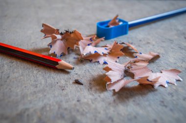 Bir kalem ile bir kalemtıraş kalem kabukları ile bilenmiş. Diğer kalem ucu kırık ve masanın üzerinde yatan