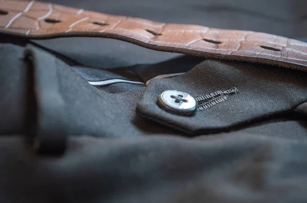 Close up of the button of a grey formal pant with a brown leather belt
