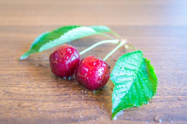 Freshly picked up red ripe cherries with leaves kept on a wooden table with water sprinkled on them.