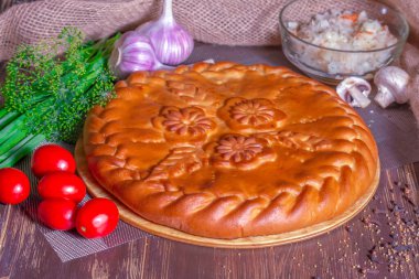 Tahta bir masada patatesli turta, yeşilliklerin, mantarların ve domateslerin yanında.