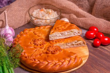 Tahta bir masada patatesli turta, yeşilliklerin, mantarların ve domateslerin yanında.