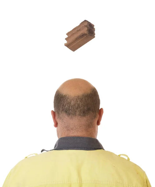 A brick falling from height towards a workers head which is uncovered and not protected.