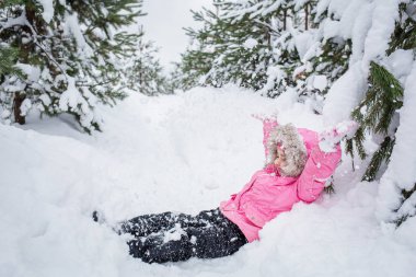 Kış çam ormanı içinde mutlu bir çocuk. Bebek kız pembe ceket kar açık atar.