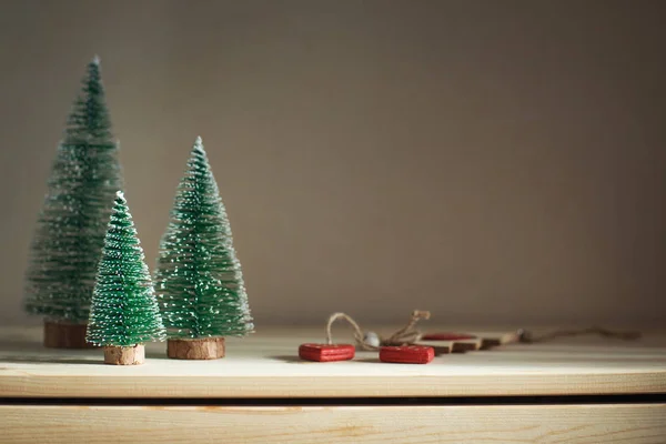 three Christmas trees on a wooden dresser. Cozy home winter still life. Toned, copy space.