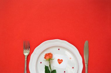 Sevgililer Günü'nde akşam yemeği. tabak, çatal bıçak takımı, gül ve kart kırmızı zemin üzerine. Alan, kopyalama minimalizm.